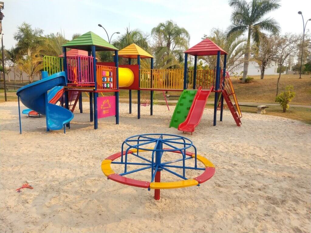 Parque infantil com escorregadores coloridos, estrutura de brinquedos em parque ao ar livre, cercado por árvores e areia, ideal para crianças.