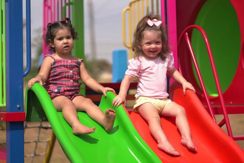 Duas crianças brincando em escorregadores coloridos em um parquinho ao ar livre, sorrindo e se divertindo em um dia ensolarado.